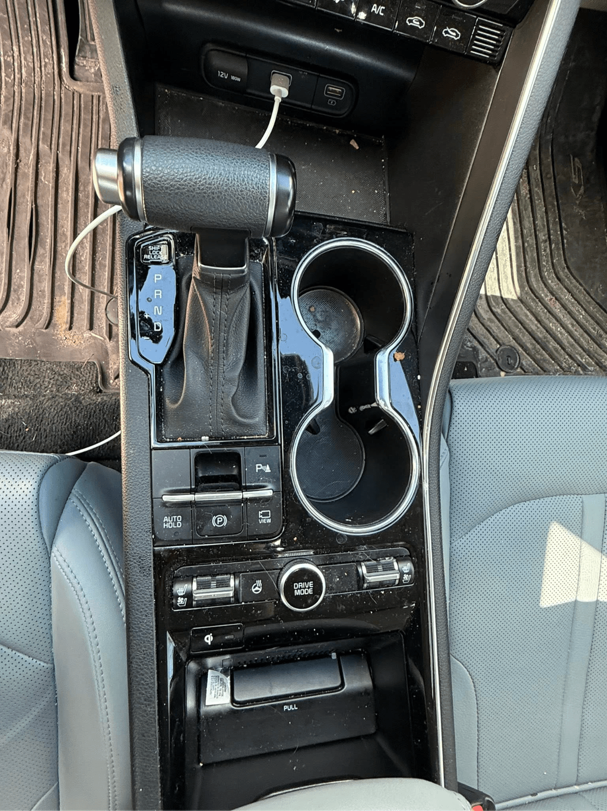 Center console with charging cables, dust, and debris in the cup holders before mobile detailing
